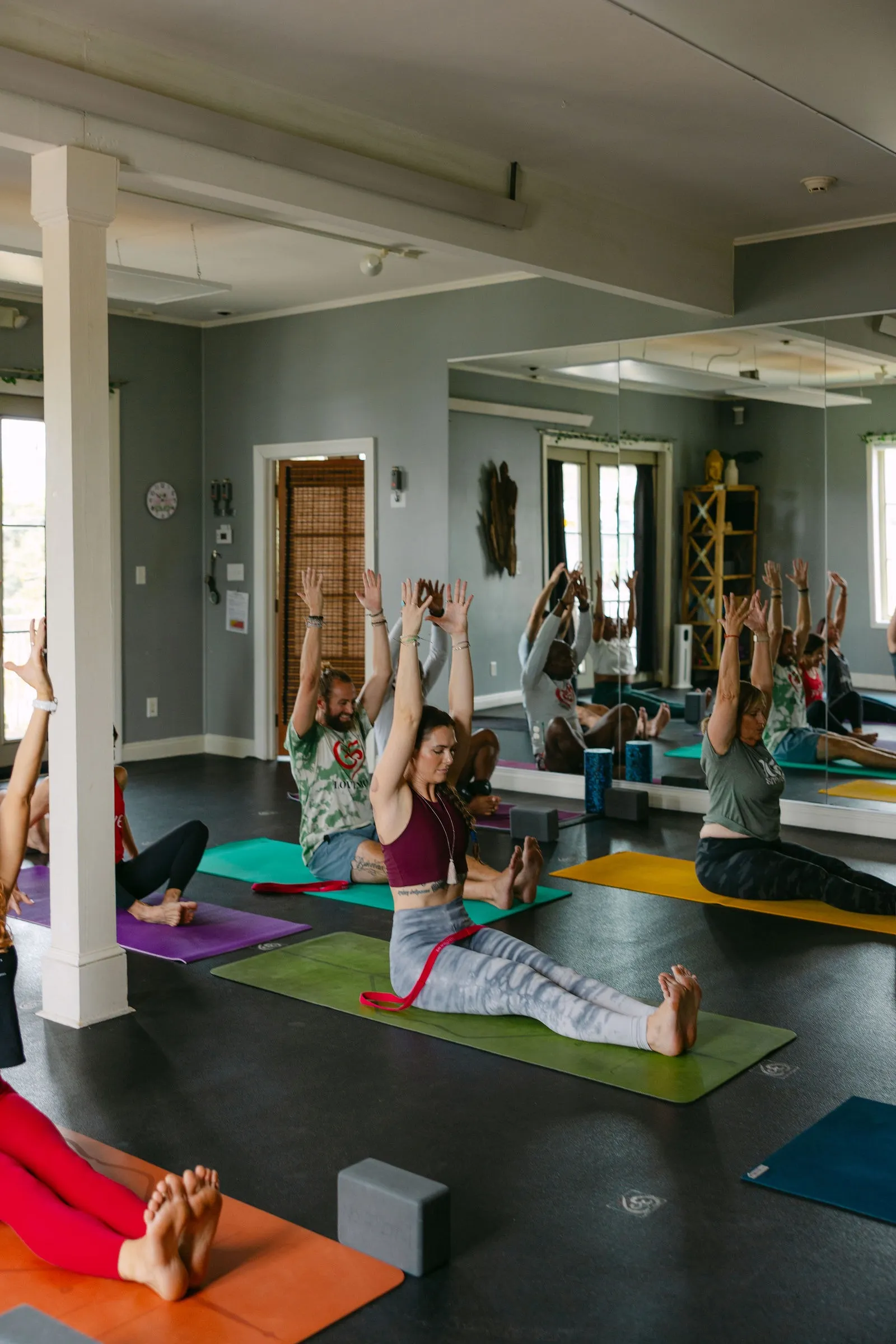 Love More students seated on colorful mats, arms raised in a studio class